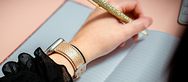 Un main qui écrit avec un stylo et un bracelet brillant